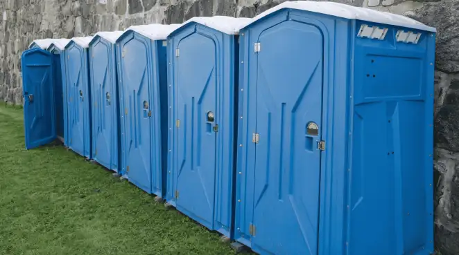 Row of blue portable toilets lined up on grass against a stone wall for event sanitation in Knoxville, TN