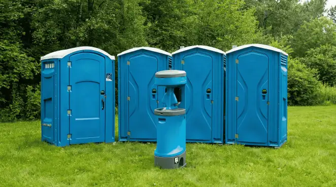 Four blue portable toilets and a matching hand washing station on grass near trees, a common sight at local outdoor events in Knoxville, TN