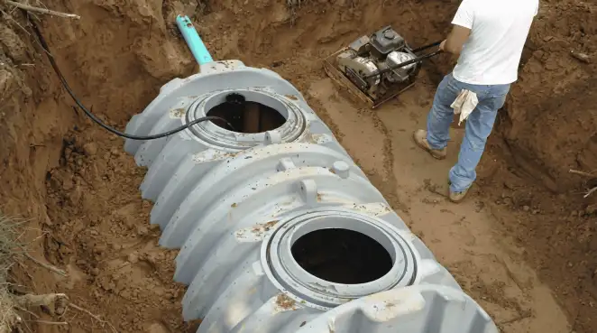 Septic tank installation showing a technician compacting soil around a new poly septic tank in an excavation pit in Knoxville, TN
